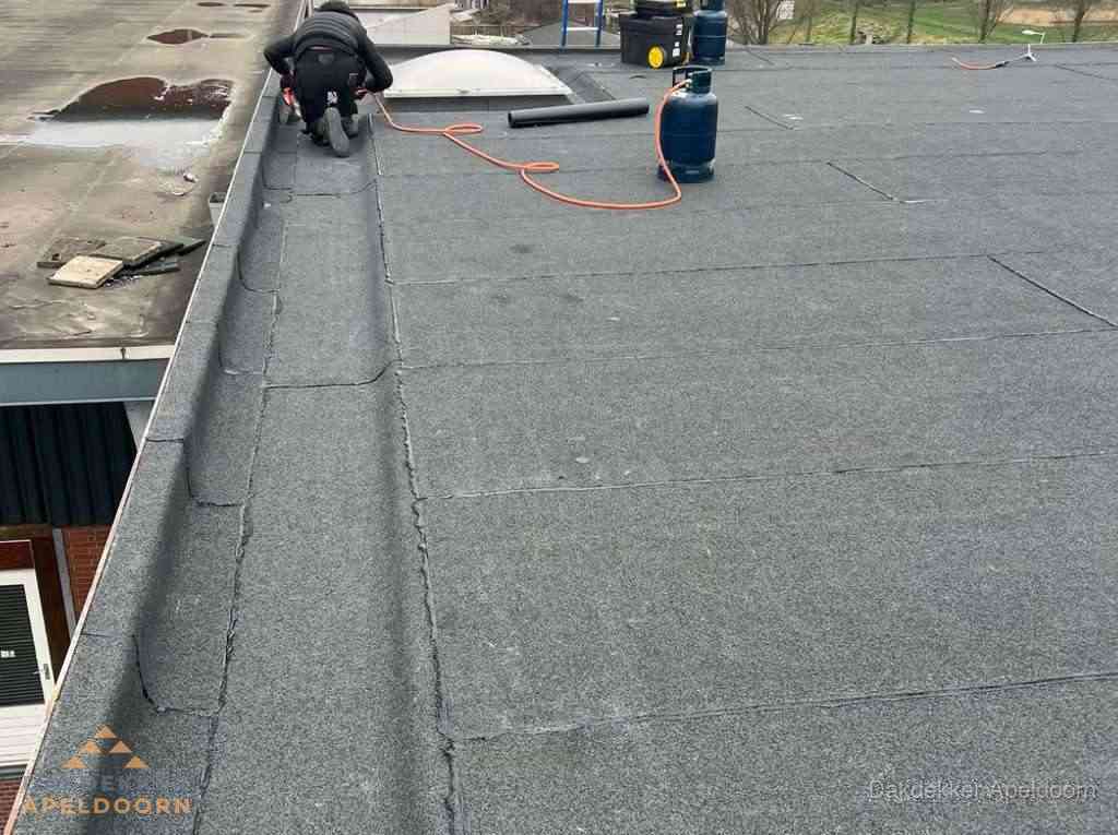 Dakdekker repareert bitumen dakbedekking op groot plat dak in Apeldoorn